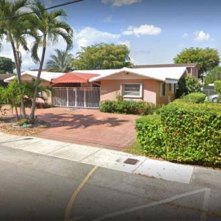 A suburban house with a red-roofed entrance, surrounded by palm trees and well-maintained landscaping.
