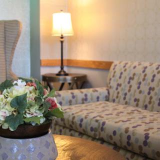 A cozy living room setup featuring a floral couch, a decorative lamp, and a charming flower arrangement.