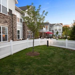 A landscaped residential area with a white fence and a tree in front of an apartment building.