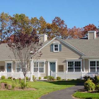 A suburban house with a well-maintained yard and autumn trees in the background.