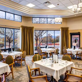 A well-appointed dining area with neatly arranged tables and chairs, large windows, and elegant lighting.