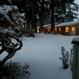 A serene winter evening, with a cozy house glowing warmly amidst a blanket of fresh snow.