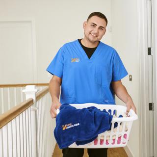 A person in a blue uniform holding a laundry basket indoors.