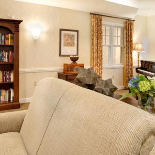 A cozy living room with elegant decor, featuring a sofa, bookshelf, piano, and warm lighting.