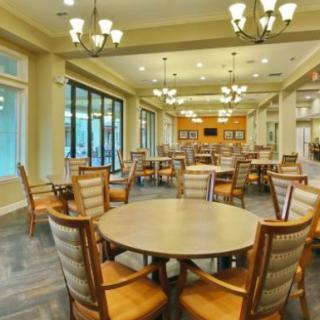 An elegantly lit dining area with multiple tables and chairs, featuring large windows and chandeliers.