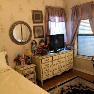 A cozy vintage-style bedroom featuring a dresser with a TV, decorative mirror, and elegant curtains.