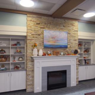 A cozy living room featuring a stone fireplace with decorative shelves and artwork above.