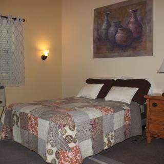 A cozy bedroom with a quilt-covered bed, nightstand, lamp, and wall painting.