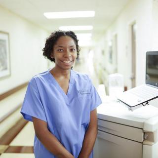 A nurse standing in a hospital corridor wearing blue scrubs.