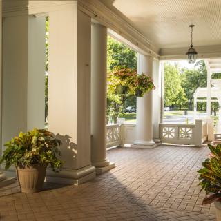 Sunny porch with columns and hanging plants.