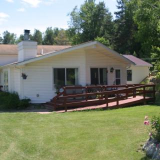 A single-story house with a wheelchair ramp, surrounded by a well-maintained lawn and trees on a sunny day.