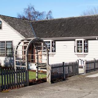 A one-story building with a garden arch and picket fence.