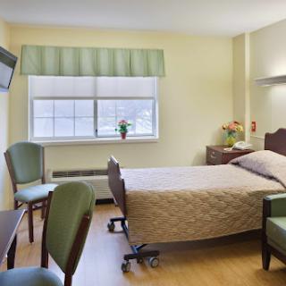 A tranquil hospital room featuring a bed, seating area, and natural light.
