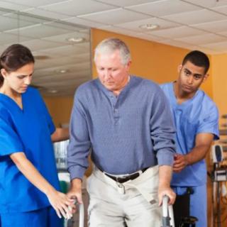 A senior man receiving assistance from healthcare professionals during physical therapy.