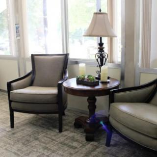 A cozy seating area featuring two armchairs, a round wooden table, and a decorative lamp by the window.