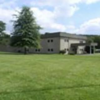 A building with a large lawn and a tree under a partly cloudy sky.