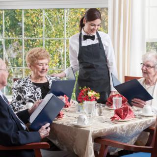 A group of seniors seated at a restaurant table with a waitress taking their order.