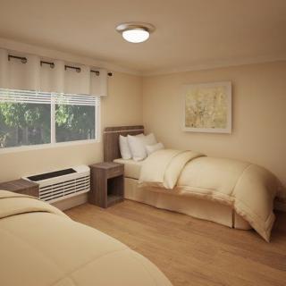 A cozy bedroom with twin beds and simple decor, featuring a window and wood flooring.
