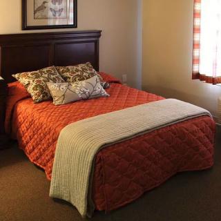 A cozy bedroom with a neatly made bed featuring an orange quilt and decorative pillows.