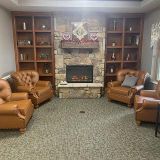 A cozy living room with a central fireplace surrounded by leather armchairs and wooden bookshelves.