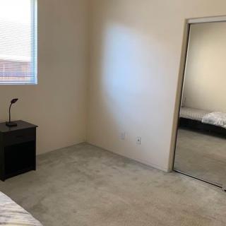 A minimalist bedroom with a bed, nightstand, lamp, and mirrored closet.