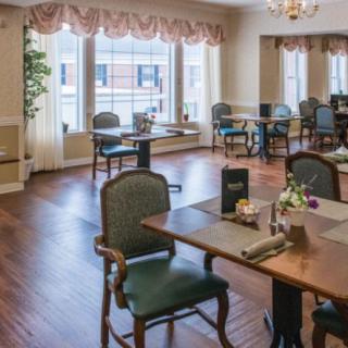 A cozy dining area with neatly arranged tables and chairs, featuring large windows and elegant decor.
