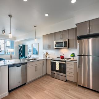 A modern kitchen with stainless steel appliances, sleek cabinets, and wood flooring.