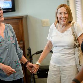 Two women smiling and holding hands indoors.