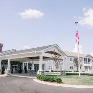 A sunny day view of a building entrance with a flagpole and well-maintained landscaping.