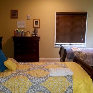 A cozy bedroom with a bed and dresser, featuring warm colors and decorative elements.