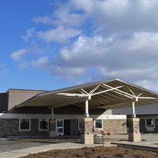 A modern building entrance with a distinctive roof design under a partly cloudy sky.