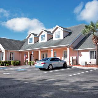 A residential building with a parking lot and a car under a blue sky with clouds.