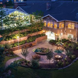 A serene garden view at night, illuminated by soft lights with seating areas and lush greenery.
