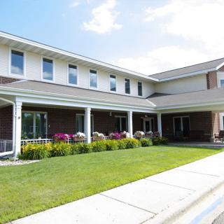 A residential building with a well-maintained lawn and colorful flowers under a partly cloudy sky.