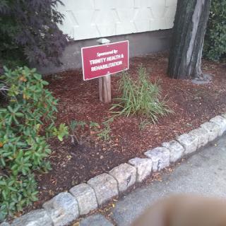 A warning sign placed in a landscaped area, surrounded by plants and decorative stones.