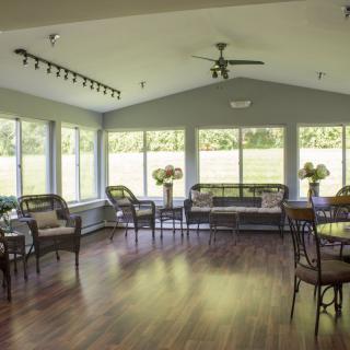 A bright and spacious living room with large windows, featuring several chairs, a table, and a wooden floor.