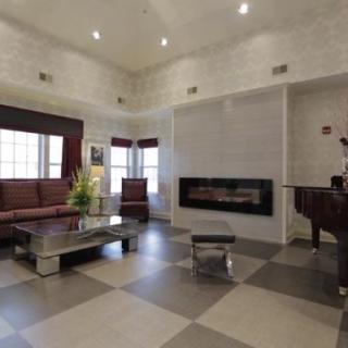 A modern living room with a fireplace and grand piano, featuring high ceilings and neutral-colored tiles.