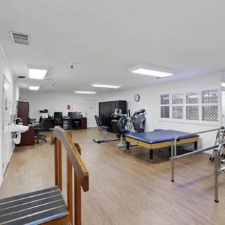 A spacious physical therapy room equipped with exercise machines, rehabilitation bars, and a workspace.