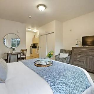A cozy bedroom featuring a neatly made bed, dresser with a TV, and a small dining area.