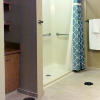 A bathroom featuring a shower with a patterned curtain, handrails, and towel rack.