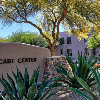 A healthcare center building surrounded by lush plants and trees.