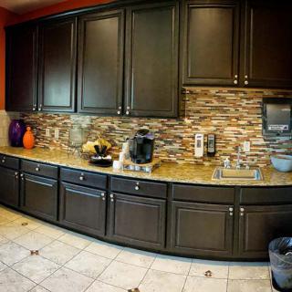 A modern kitchen with dark cabinets, a stone backsplash, and various appliances on the countertop.
