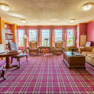 A classic living room with plaid carpet, wooden furniture, and cozy seating by large windows.