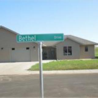 A suburban street with a green street sign labeled 'Bethel' in front of a single-story house.