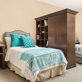 A cozy bedroom with twin beds, featuring teal accents and a wooden bookcase.