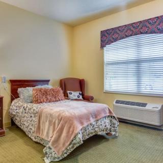 A cozy bedroom with a single bed, armchair, and large window.
