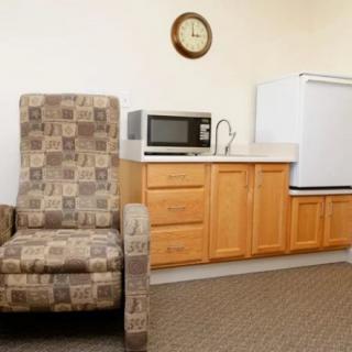 A cozy kitchenette with a patterned armchair, equipped with a microwave and fridge.