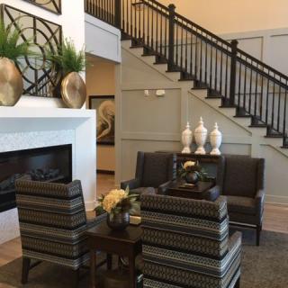 A modern living room featuring a cozy seating area with striped chairs and a sofa, accented by decorative vases and a staircase in the background.
