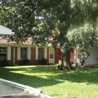 A suburban brick house with a well-maintained lawn and large tree in the front yard.
