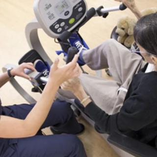 A therapist assisting a patient on a stationary exercise bike during a rehabilitation session.